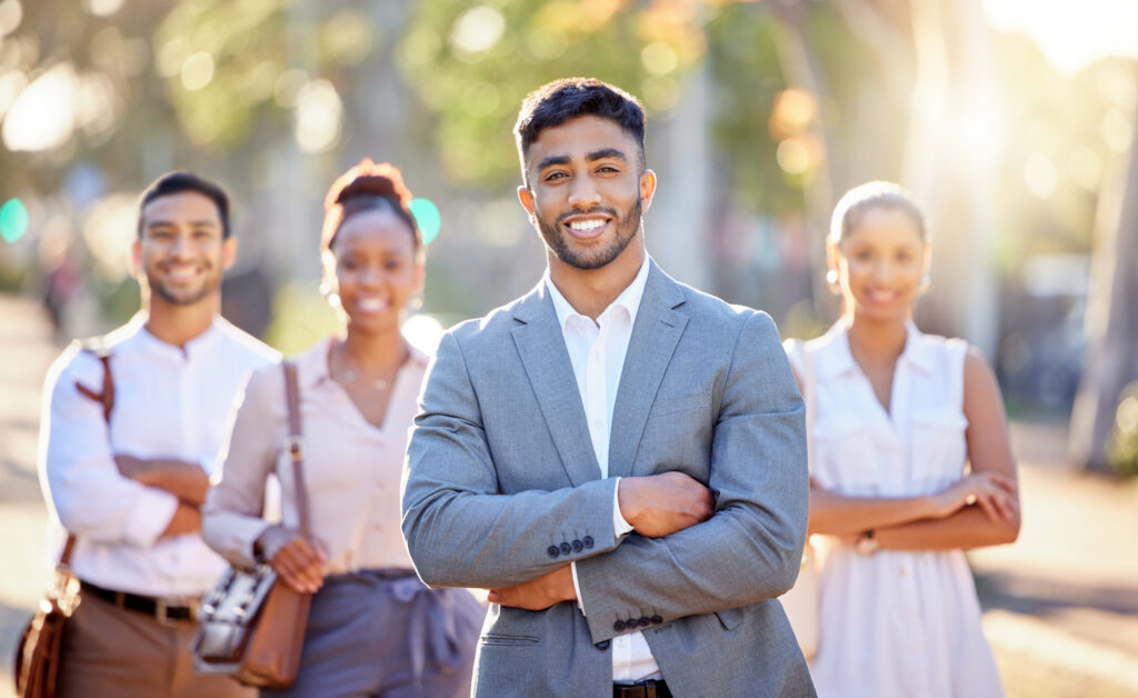 A group of young professionals standing confidently with their arms crossed in a bright, outdoor setting.